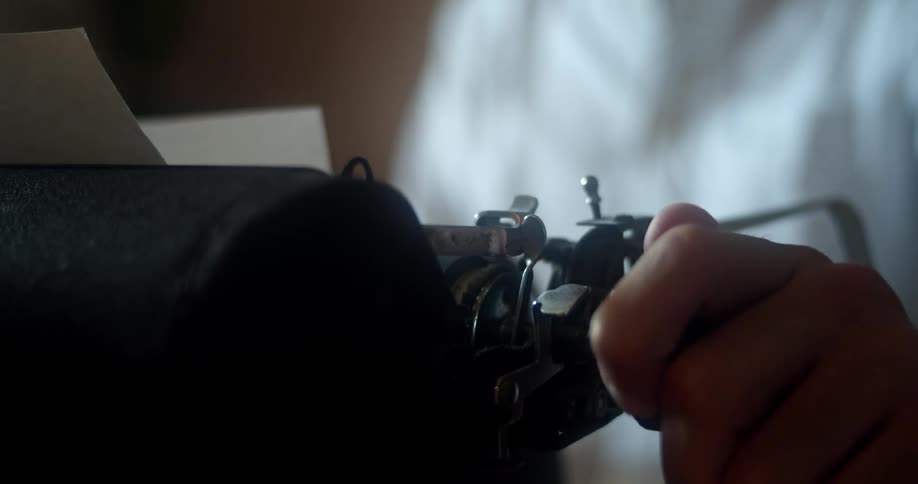 Man with a white shirt sits at a desk and uses a old black typewriter