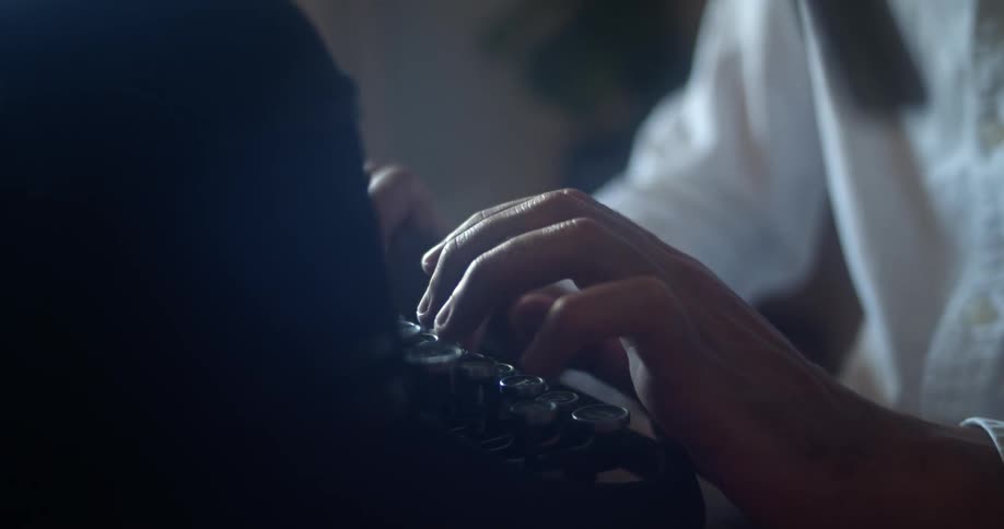 A person with a white shirt sitting and typing on a typewriter