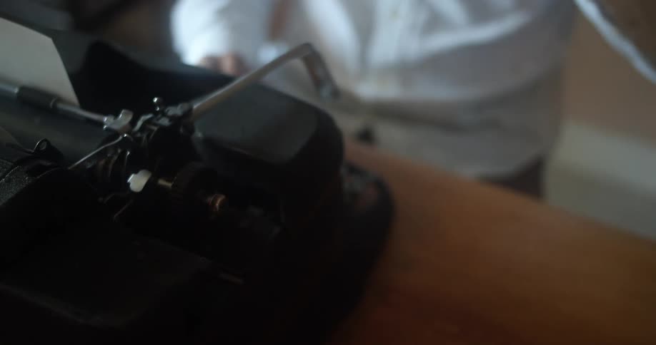 A person typing on a typewriter pauses for a moment to take a sip from a coffee mug