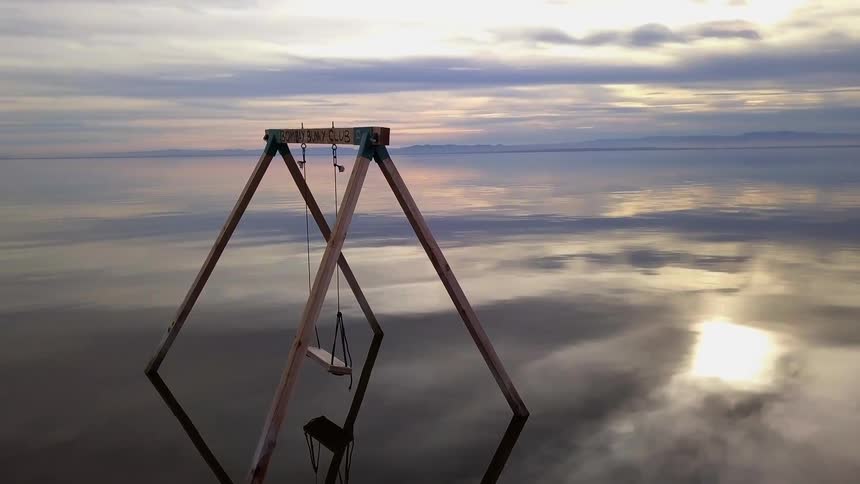 A swing set in the middle of a lake at sunset