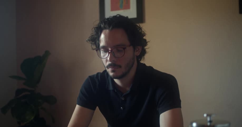 A man sits in his office and uses his phone before opening his laptop