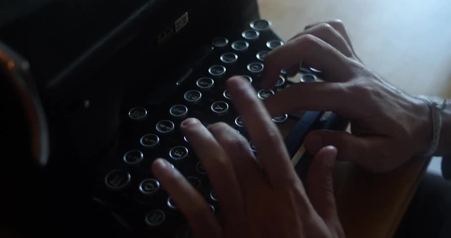 Mans hands use an old black typewriter