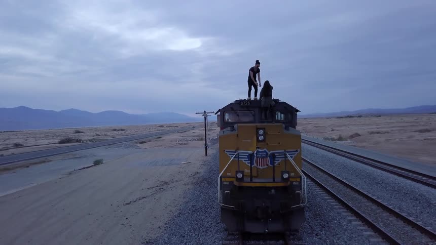 A man helps a woman to climb onto the roof of a train stopped on its tracks in the desert