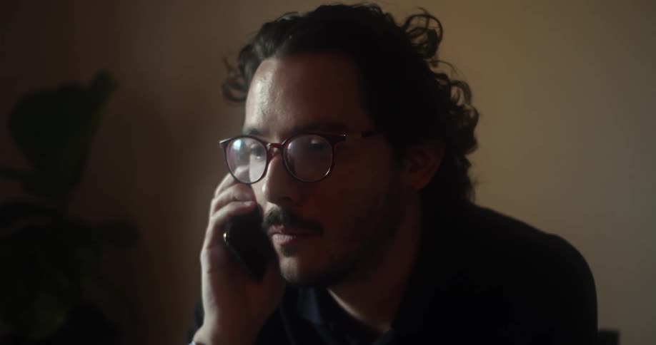 A man is sitting in a room and talking on a cellphone