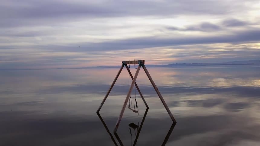 A swing set in the middle of a rippling lake at sunset