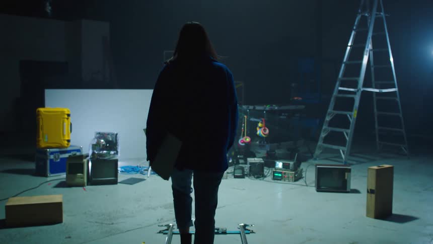 A woman walking backstage with a notepad in her hand with a ladder and lights in the background