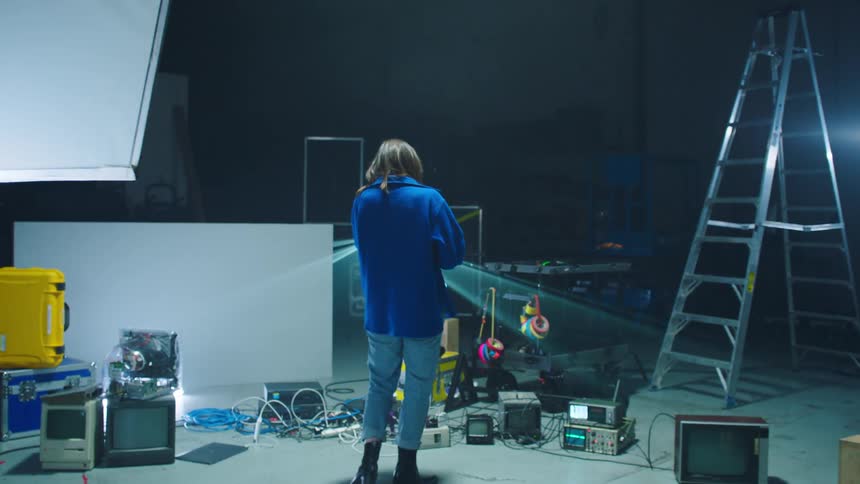Men set up equipment in a studio while a woman makes notes in a book