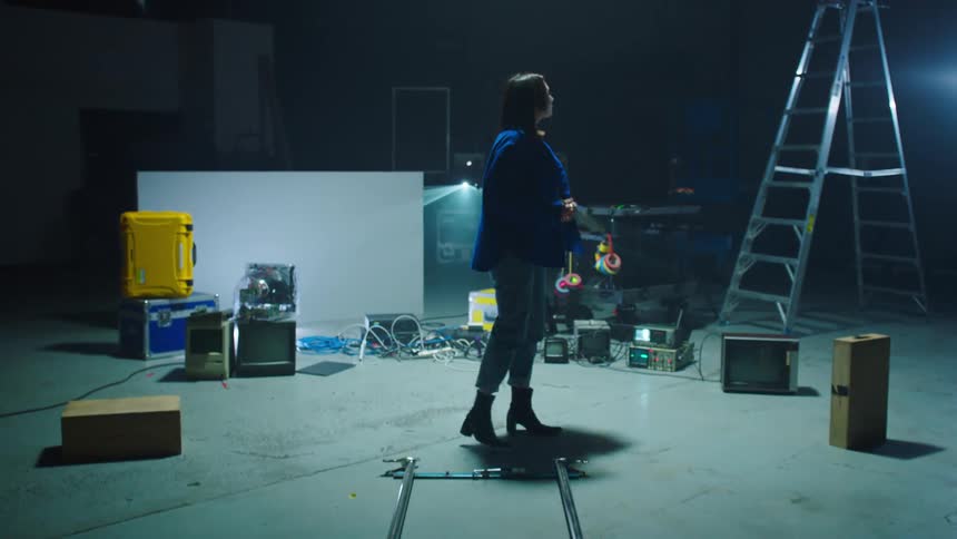 A woman with a pen and a pad walking and writing backstage with a ladder in the background