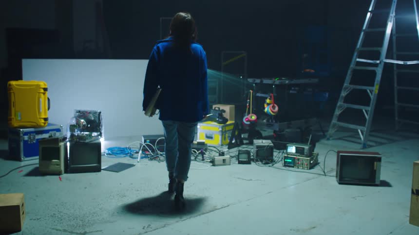 A woman with a notebook and a pen walking backstage with a ladder and lights in the background