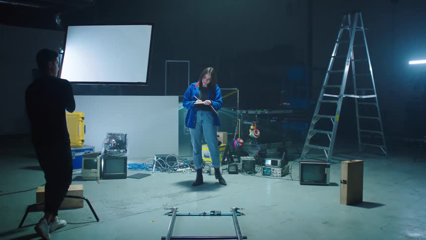 A woman with a pen and notebook writing backstage with lights and a ladder