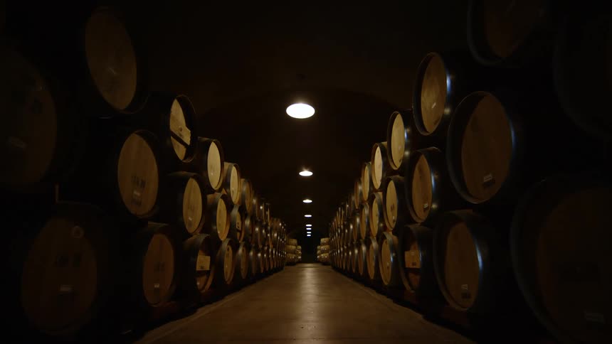 A walkway between rows of stacked barrels in a dim warehouse