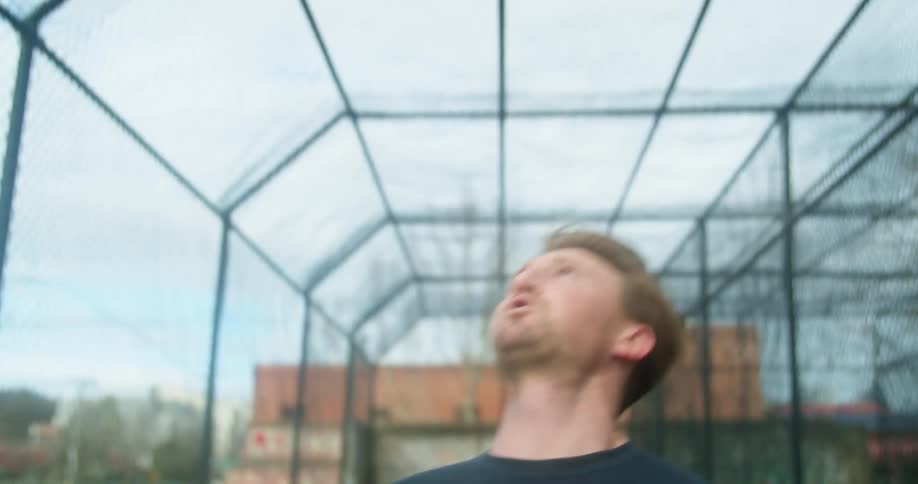 A man tosses a weighted medicine ball as he works out in a fenced in area at a park