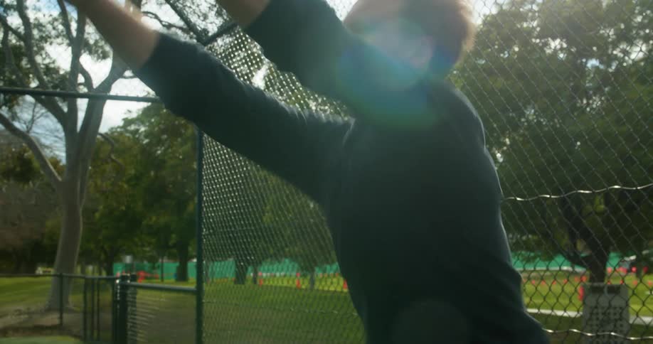 Young man in fenced in area of park throws basketball toward goal