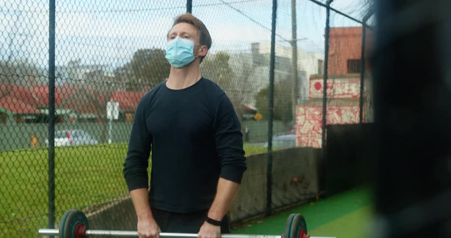 A man is lifting weights outdoors while wearing a mask