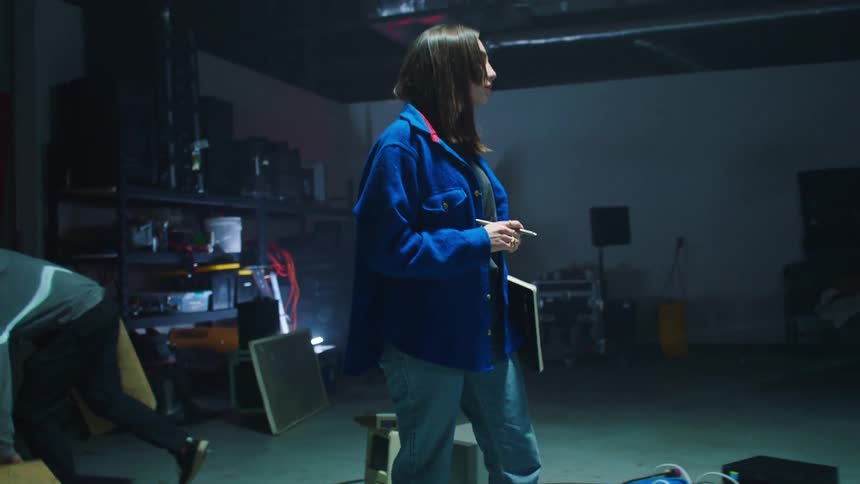A woman takes stock of inventory while men set up equipment for a performance