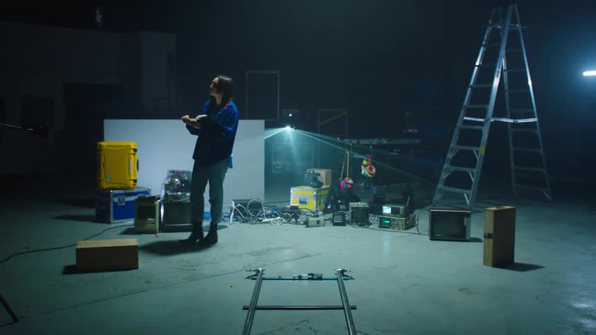 A woman with a book and a pen writing and walking backstage with a ladder in the background