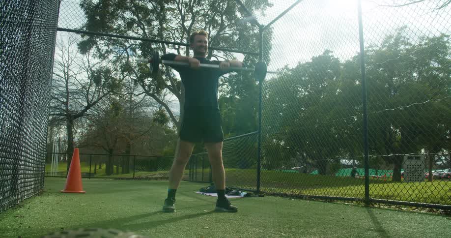 A man lifts weights in a fenced in area at a public park