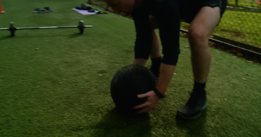 A man in a public park throws a weighted ball as he exercises