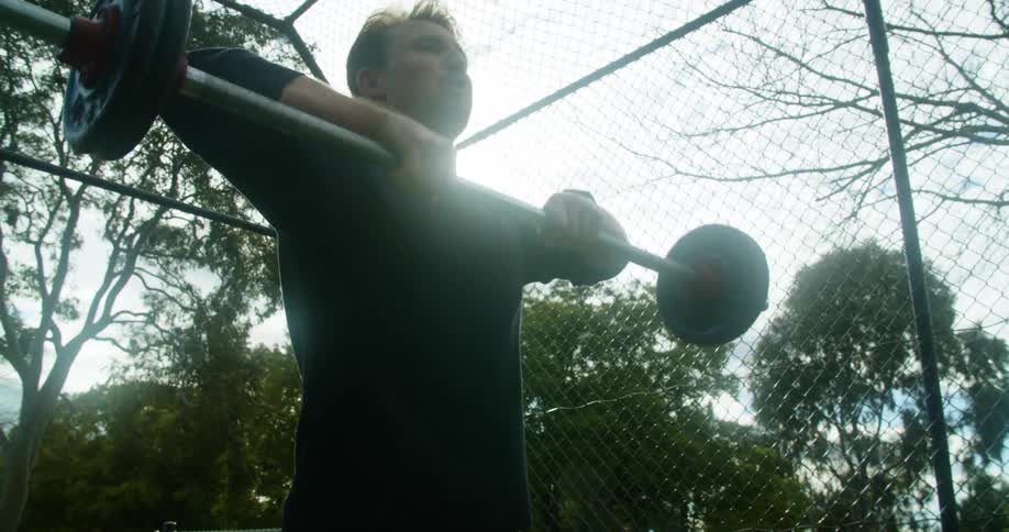 A man picks up a bar with small weights on it and lifts it upwards repeatedly