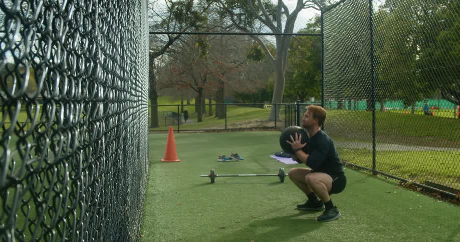 A man throws an exercise ball at a cage and then picks it up when it falls to the ground