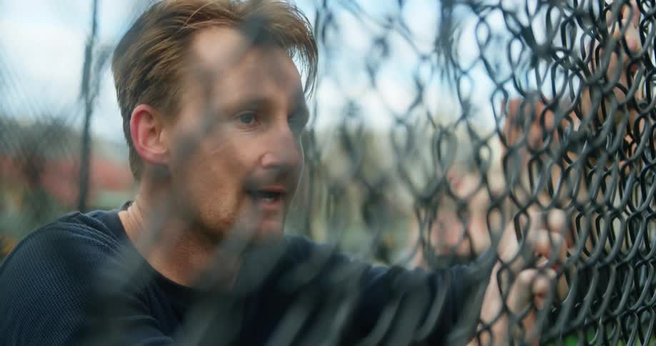 A young man leans on a fence as he catches his breath and looks at his watch