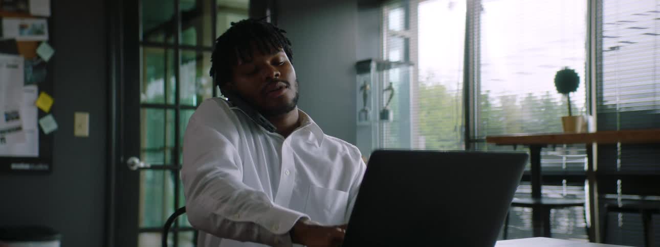 Young man working from home on a laptop takes a call on a smartphone
