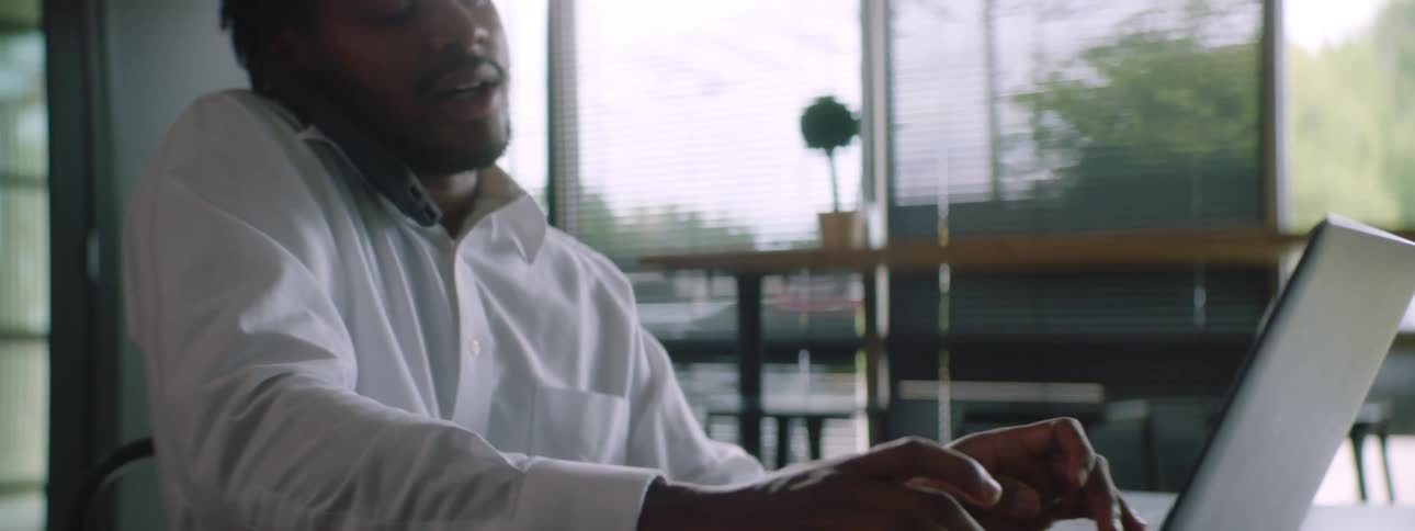 A man in an office talks on his cell phone while typing on his laptop