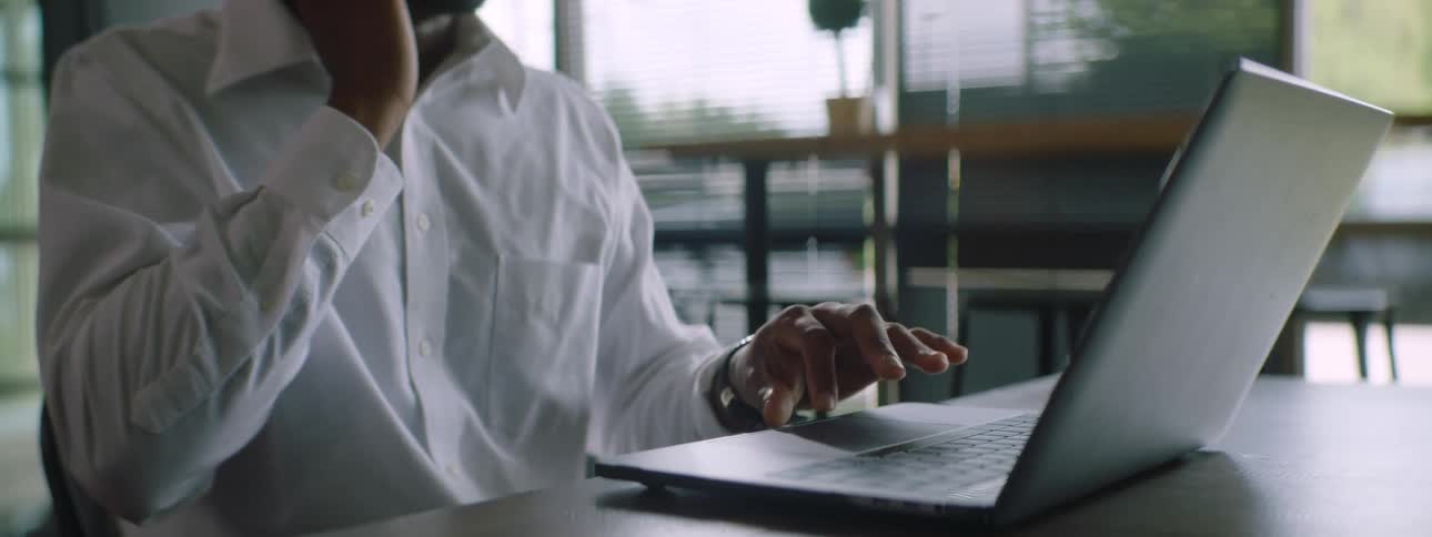 A man sits at a desk with a laptop and talking on a cell phone