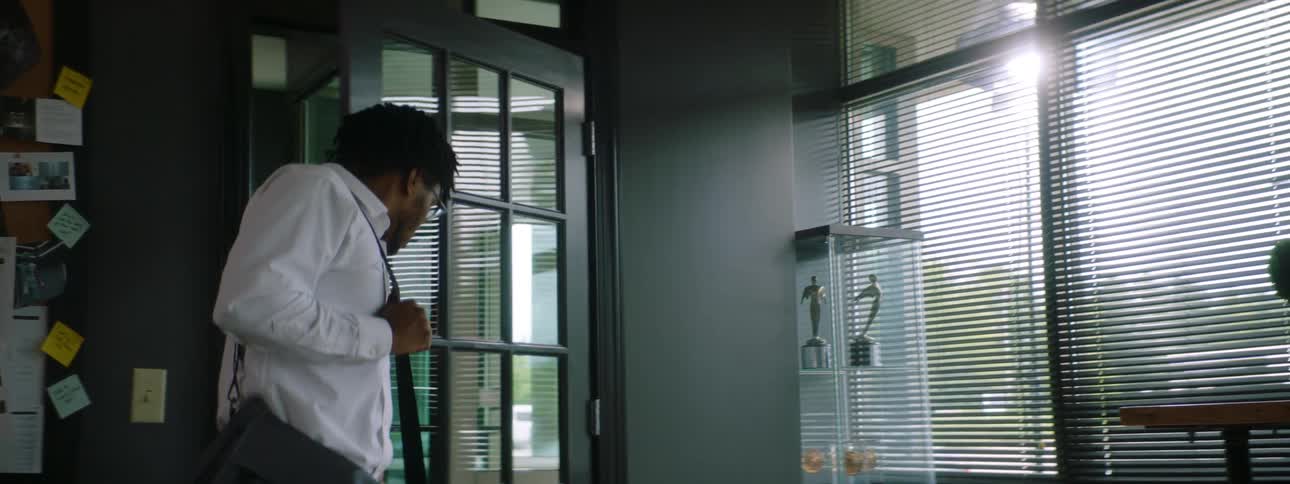 A man walks into an office and places a bag on the floor as he sits down in a chair at a table