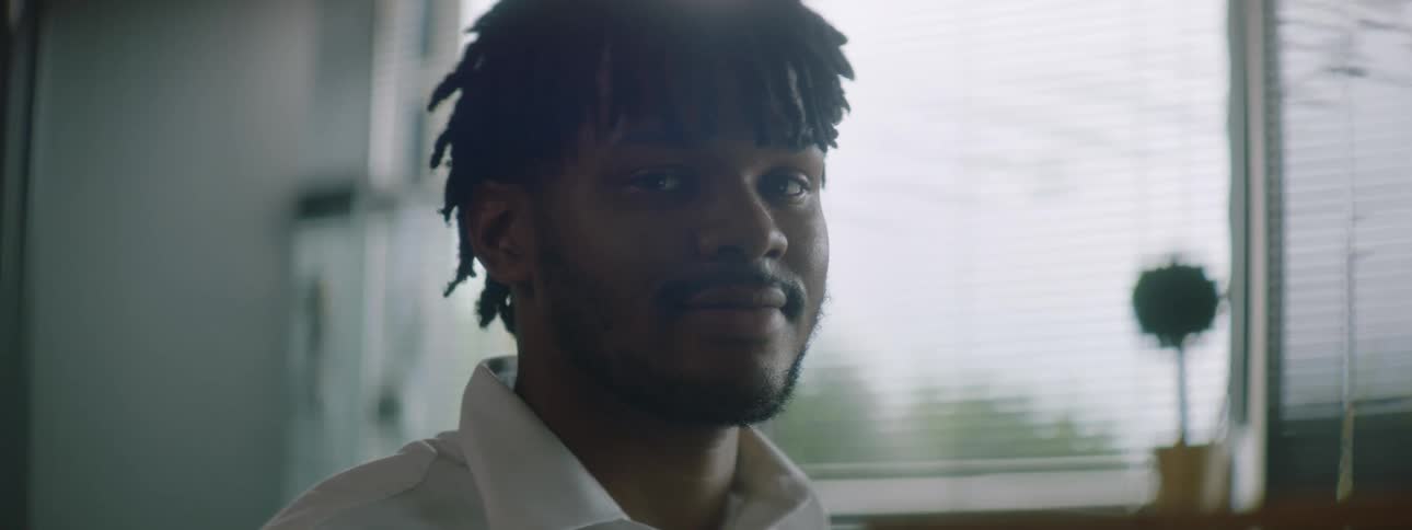 A black man smiles while sitting in an office