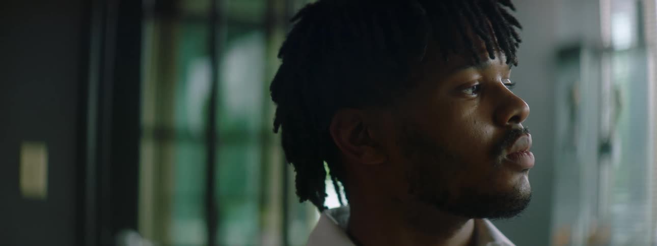 A man with a white shirt in a room with windows and blinds in the background