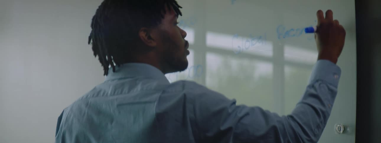 Young man writes on a whiteboard with a blue marker in a room