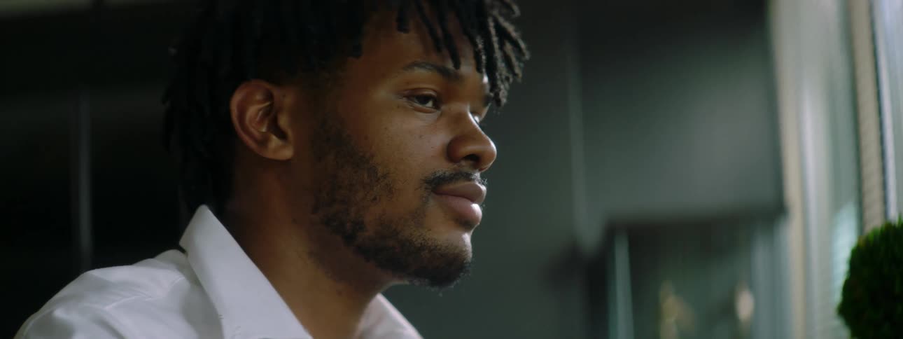 Black man with braids a beard and a white shirt drinks a cup of coffee and uses a tablet