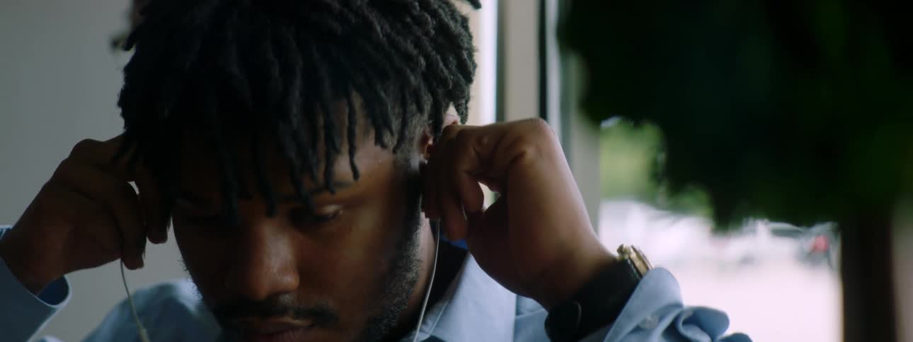 Man with braids a beard and a blue shirt wears earphones