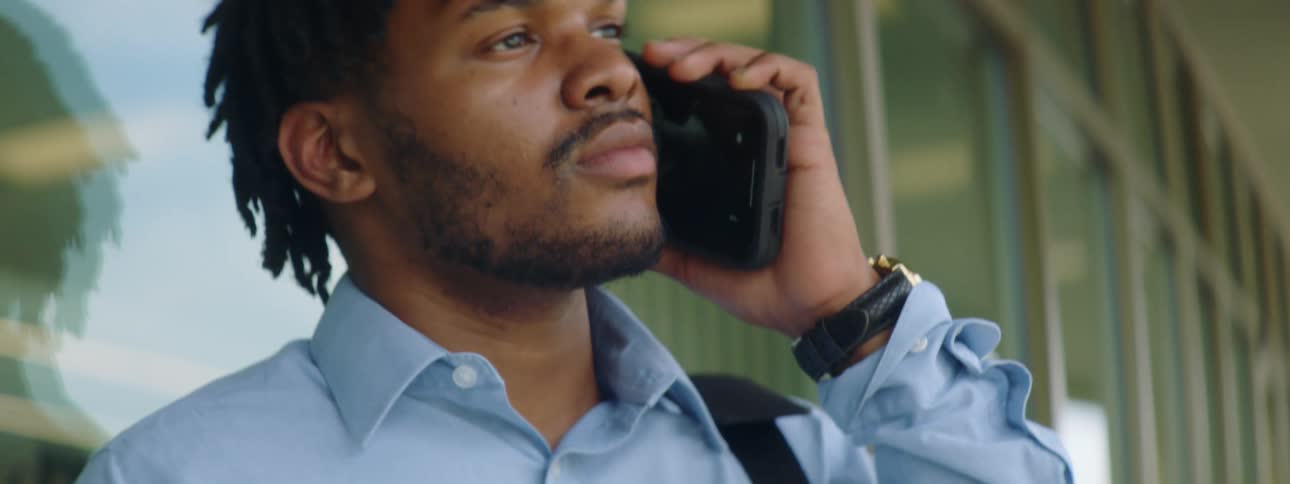 Black man with braids and a blue shirt makes a phone call with a smartphone