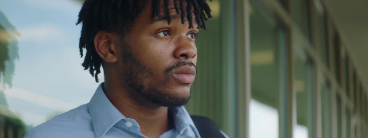 Black man with braids a beard and a blue shirt looks at his smartphone and thinks about something