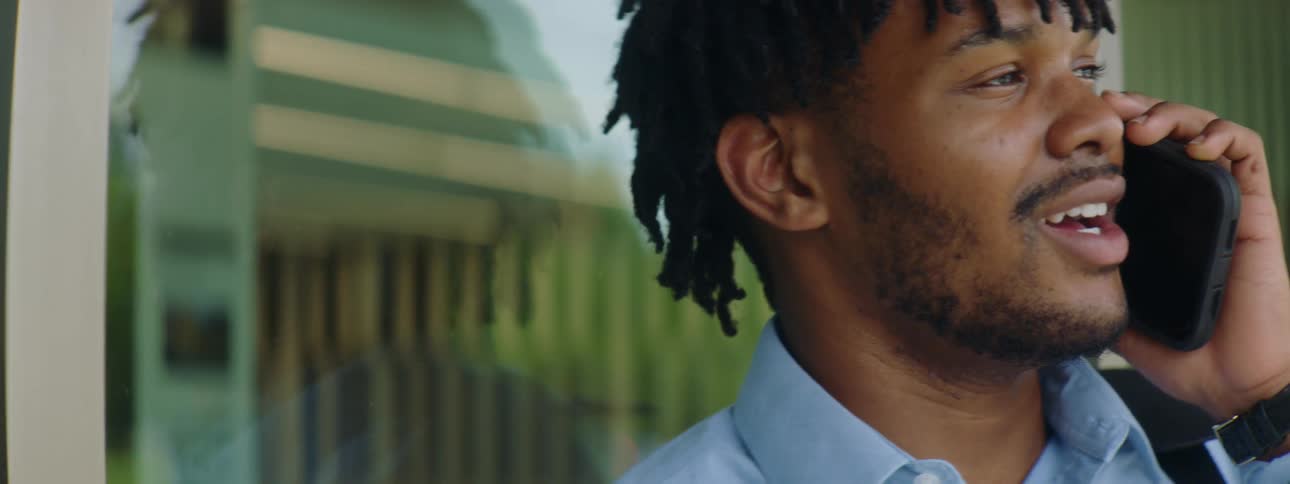 Black man with a beard braid hair and a blue shirt talks on the smartphone