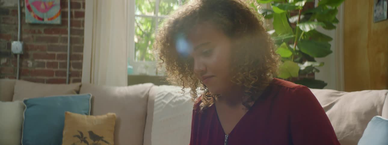 A young woman sits on a couch and types on a laptop