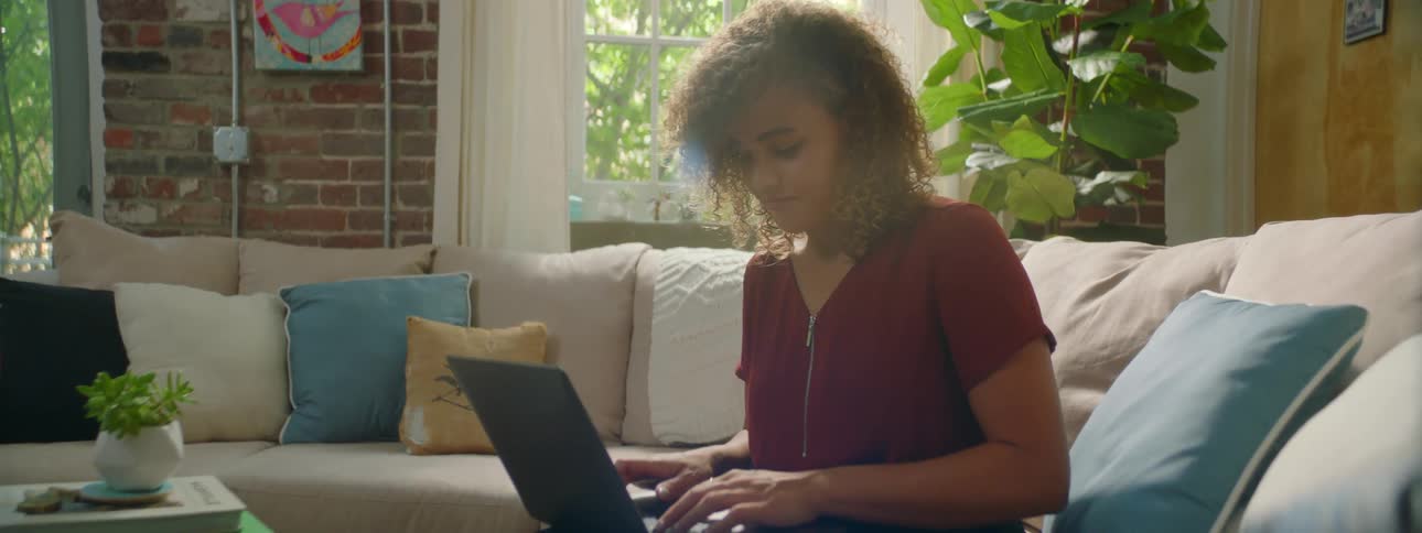 A woman in a room sitting on a couch typing on a laptop