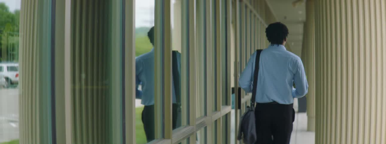 A man with a bag and a smart phone walking next to a building