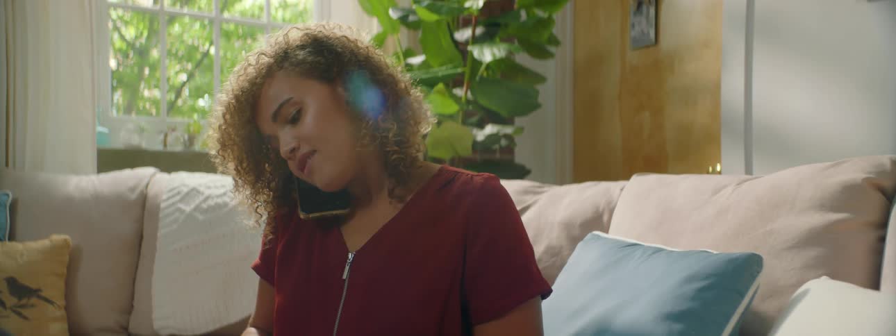 Young woman talking on cell phone and nodding while typing on laptop