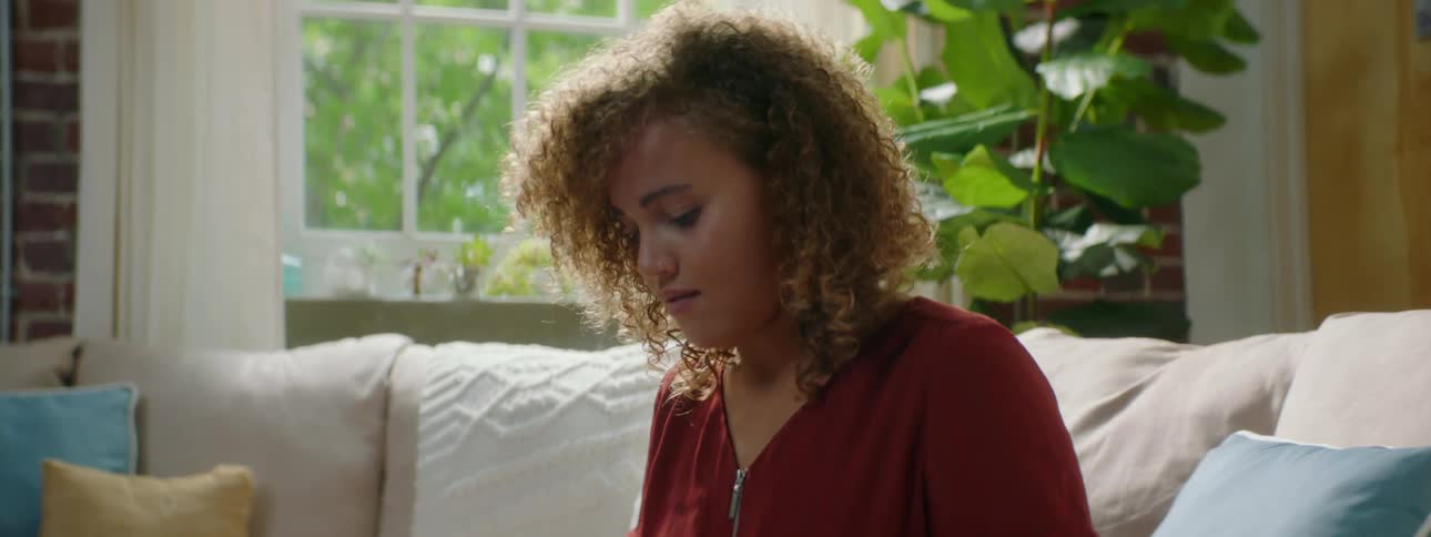 A young female sits on her home couch and types on a laptop
