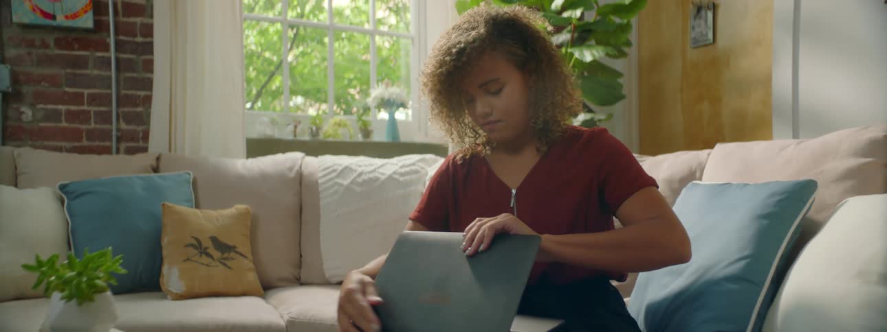Young woman sits in a couch in the living room and takes a laptop from the table