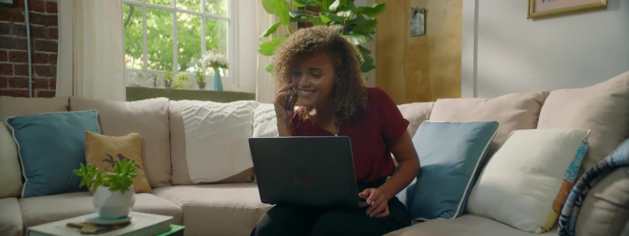 Woman sitting on couch and typing on laptop answers mobile phone