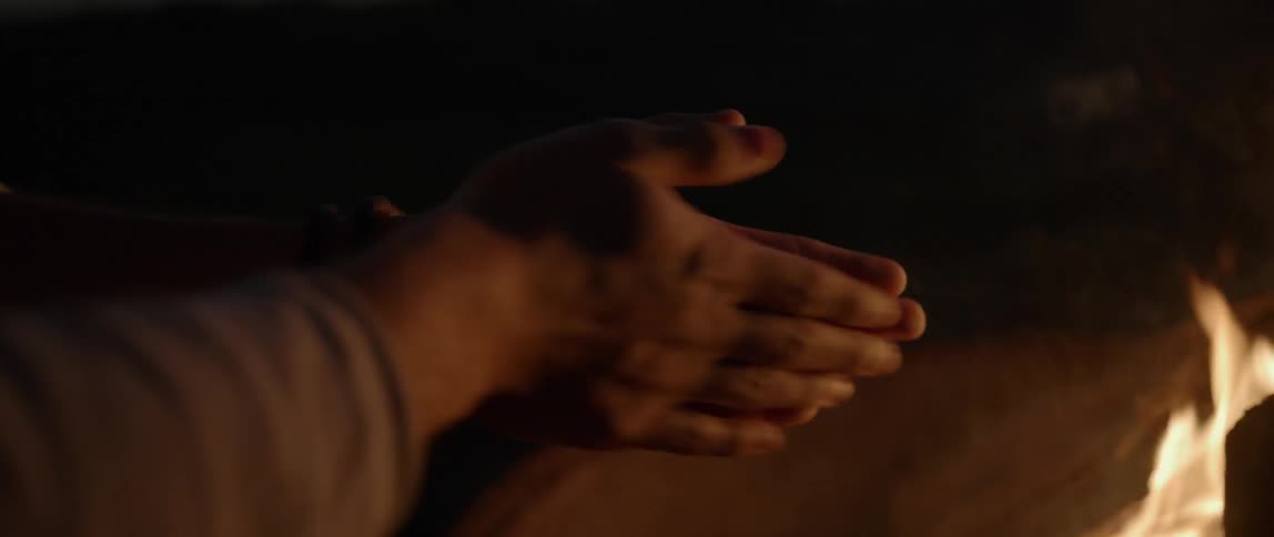 A man warms his hands by a campfire