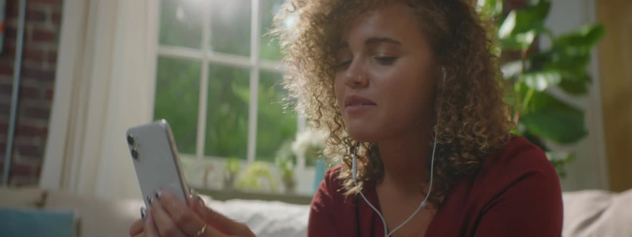 A young female sits on a couch with a cell phone having a video call