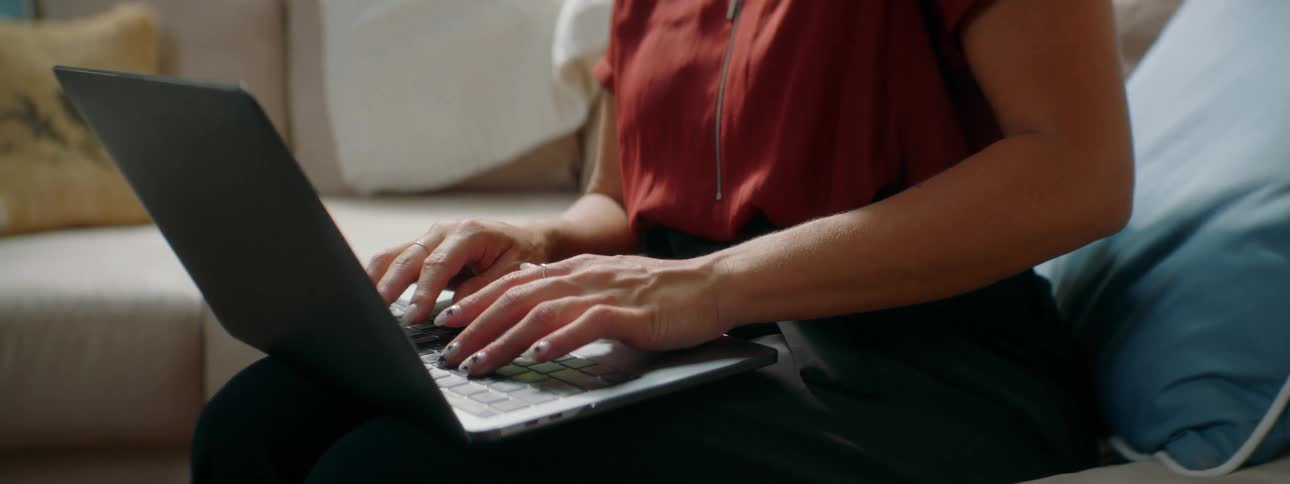 Young woman sitting in a couch at home talks on her smartphone while using a laptop