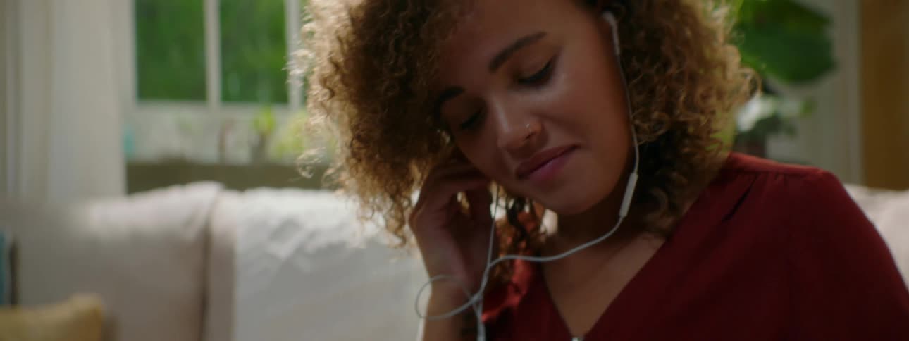 A young woman places earbuds in her ear before using the smartphone the earbuds are connected to