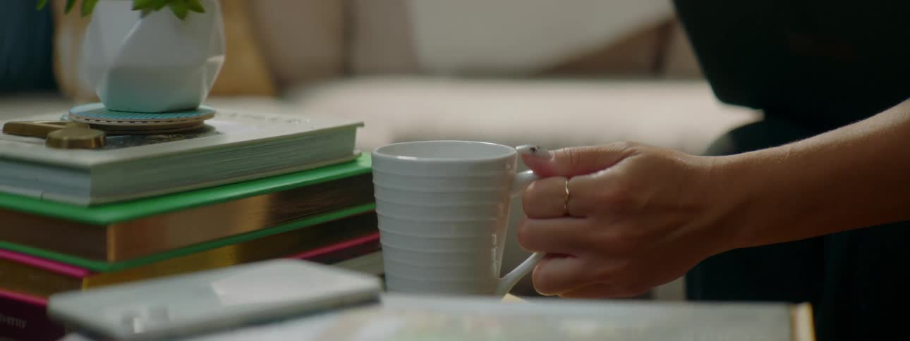 Coffee mug being placed next to stack of books on table