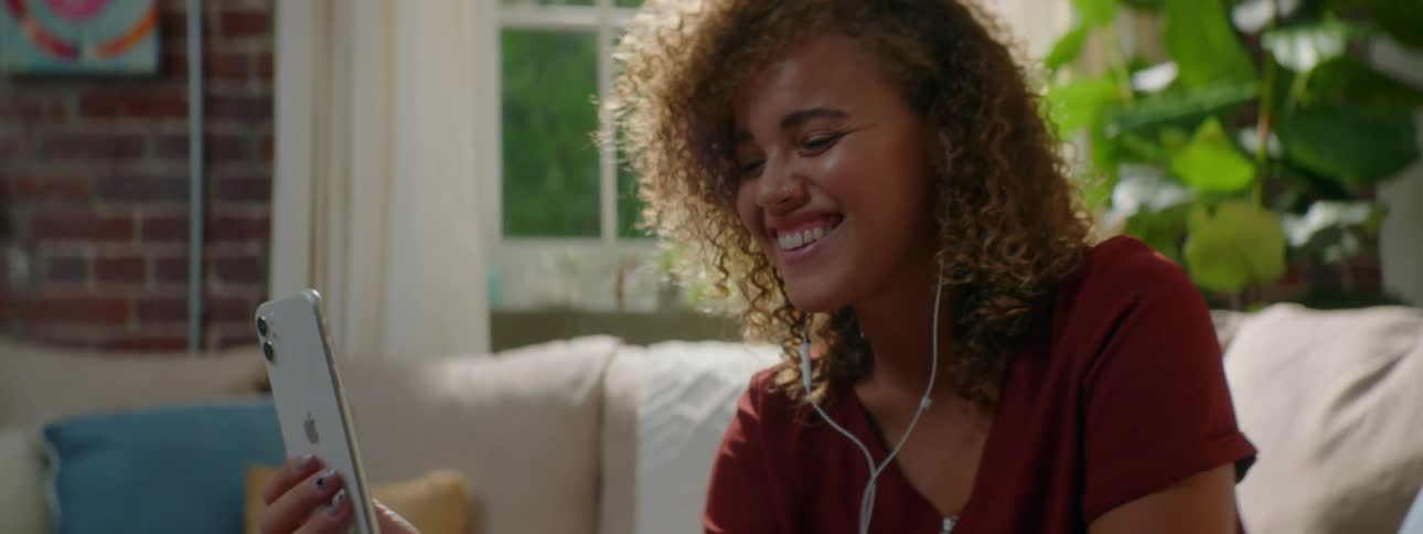 Woman with curly hair and a red blouse makes a video call on smartphone in the living room at home